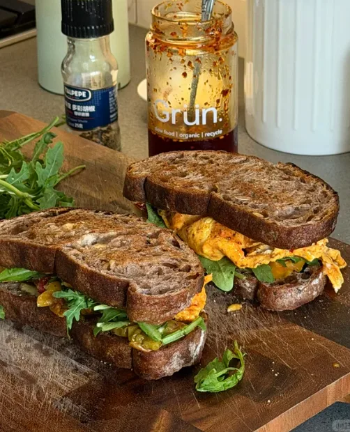 Two toasted bread sandwiches filled with egg and greens on a wooden board.