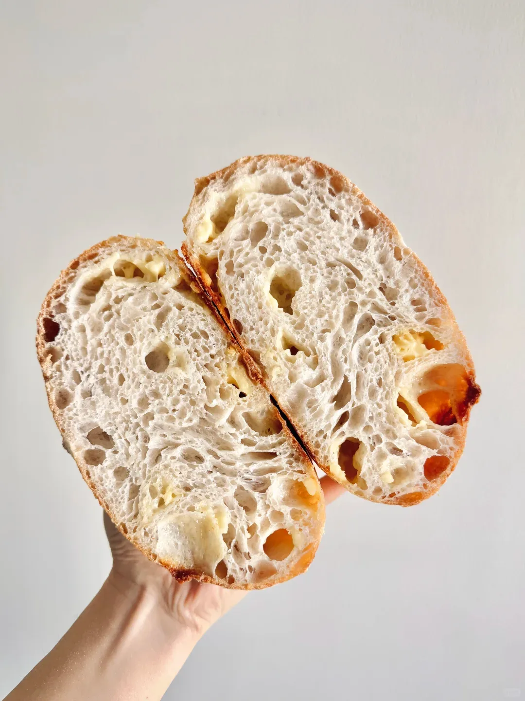 A hand holding two halves of a loaf with a light, open crumb and golden pieces throughout.