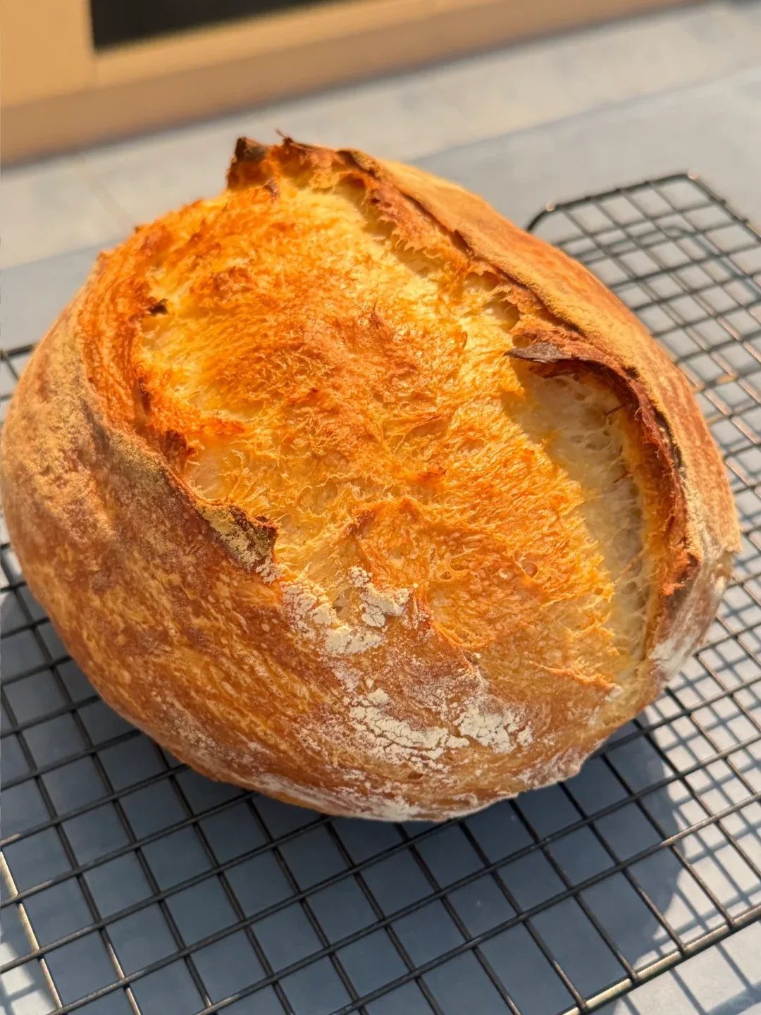 A golden round loaf with an open score cooling on a wire rack.