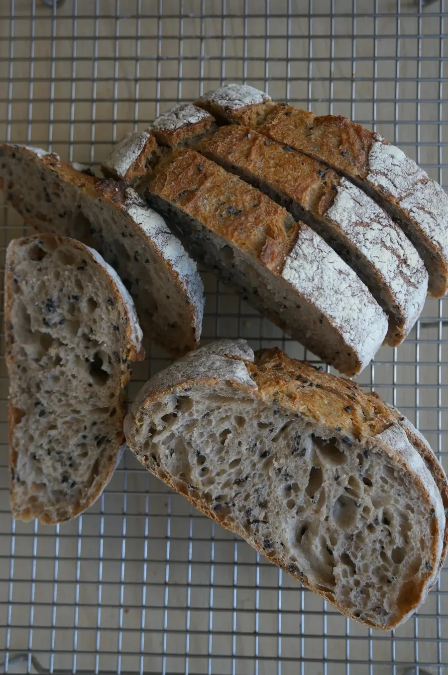 Slices of a golden, flour-dusted loaf showing the crumb on a cooling rack