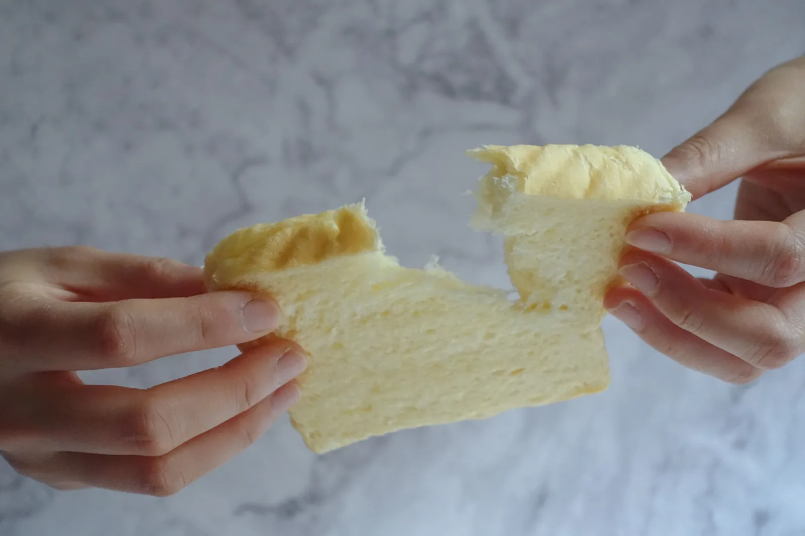 Two hands pulling apart a soft piece of white bread, revealing its delicate crumb.